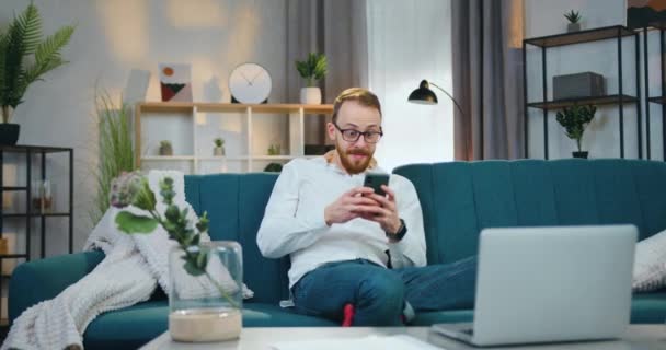 Attraktiv glad i hög sprit ung skäggig man i glasögon glädje när få goda nyheter på smartphone och lyfta händerna från lycka — Stockvideo