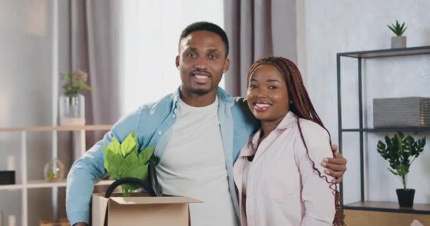 Snyggt positiv bekymmersfri ung afrikansk amerikansk par tittar på kamera med glada ansikten i omlokalisering dag till ny lägenhet, fastighetskoncept — Stockvideo