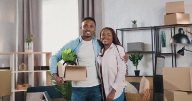 Çekici, mutlu, gülümseyen, Afro-Amerikan bir çift. Kameranın önünde birlikte aldıkları yeni dairede duruyorlar.