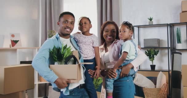 Porträtt av snygg leende vänlig kärleksfull afrikansk amerikansk familj med två små flickor som står i ny köpt lägenhet och tittar in i kameran med glada ansikten — Stockvideo