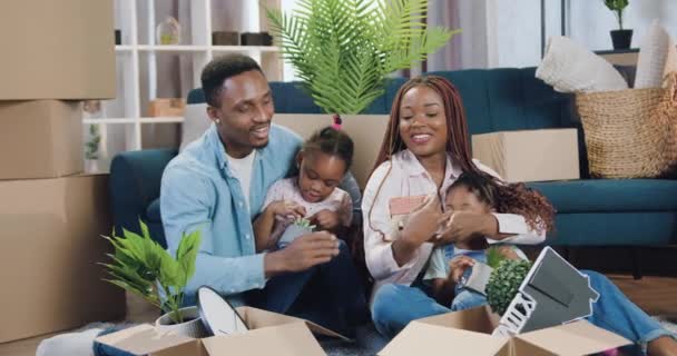Underbara glada leende afrikansk amerikansk familj med två barn njuter av sin nya lägenhet medan de sitter på golvet bland kartonger och ger höga fem varandra — Stockvideo