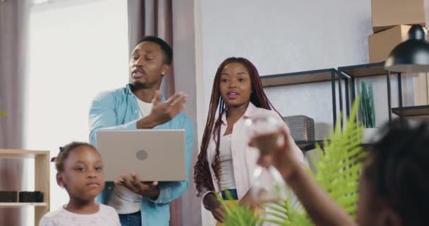 Adorable jeune couple moderne afro-américain satisfait avec des enfants debout dans leur appartement nouvellement acquis et la planification de la façon de meubler habiter à leurs préférences — Video