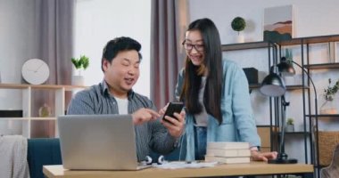 Çekici gülümseme genç Asyalı çiftin başlangıç projesi üzerinde çalışırken konuştuğu ve kullandığı akıllı telefon.