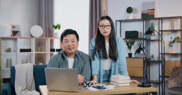 Приємна усмішка успішних молодих китайських колег чоловічої і жіночої статі, що подають на камеру під час спільної роботи над проектом стартапу в сучасному офісі — стокове відео
