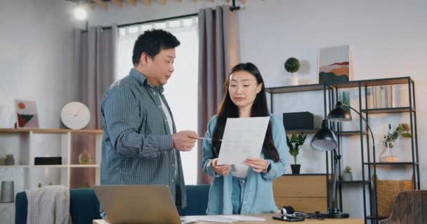 Guapo sonriendo 30-edad asiático hombre hablando con su lindo 25-edad colega femenino en contemporánea oficina habitación y discutir informe con gráficos con ella — Vídeo de stock