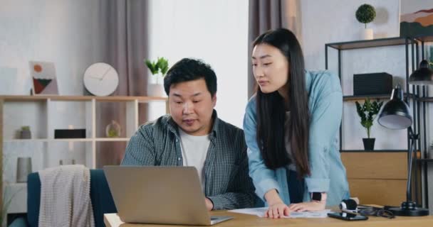 Gut aussehende zufriedene hochqualifizierte moderne asiatische Paare, die zusammen über Startup-Präsentation und Revisionsprojekt auf dem Computerbildschirm im Home Office arbeiten — Stockvideo