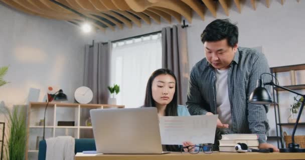 Attrayant qualifié moderne asiatique père debout près de sa fille et aider à l'université hometask sur ordinateur en utilisant rapport avec des graphiques, au ralenti — Video