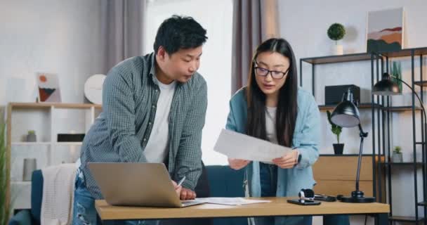 Atractivo creativo inteligente joven asiático hombre y mujer trabajando juntos en proyecto conjunto y revisioning informes con gráficos en la oficina contemporánea — Vídeos de Stock