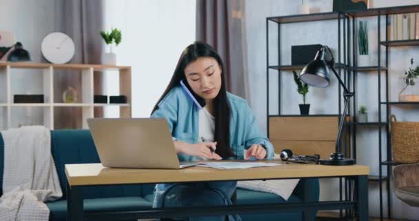 Przystojny ciężko pracujący wykwalifikowany 25-letni orientalny wygląd dziewczyna pracuje z raportów i na komputerze jednocześnie rozmawiając na telefon komórkowy, zwolnione tempo — Wideo stockowe