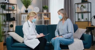 Sağlık hizmetleri konsepti, yüz maskesi takmış iyi görünümlü kadın doktor ve kadın hastayı hastalık sırasında evinde ziyaret eden beyaz kepek.
