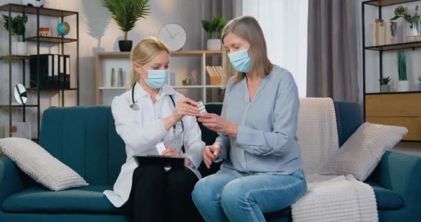 Zdravotnictví a medicína koncept, kde sympatický profesionální zkušená žena-lékař v ochranné masce dávat pilulky na její pacientky během návštěvy doma — Stock video
