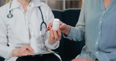 Yüz maskesi takmış çekici, deneyimli kadın doktor ve ev ziyareti sırasında kadın hastasına nasıl hap ya da vitamin alınacağını anlatan beyaz gawn.