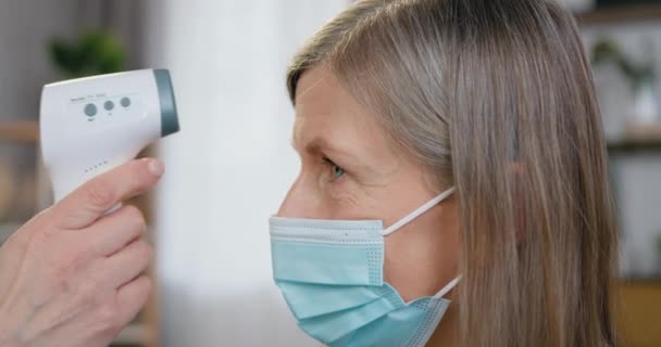 Vista laterale di una donna malata di mezza età che misura la temperatura applicando un termometro a infrarossi senza contatto sulla fronte — Video Stock