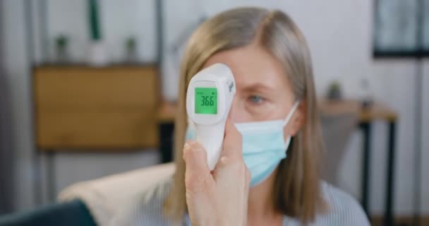 Vooraanzicht van de hand van de vrouw die infrarood-thermometer vasthoudt en 36,6 op het scherm toont na meting van de temperatuur van het lichaam van de patiënt — Stockvideo