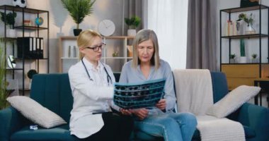 Kanepede oturan oldukça deneyimli sarışın kadın-doktor ve kadın hasta ve her ikisi de röntgen taramasına bakıyor.