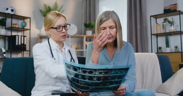 Bagus attantif wanita berusia 50 tahun duduk di sofa bersama-sama dengan dokter wanita lokal dan mendengarkan penjelasan hasil gambar x-ray — Stok Video