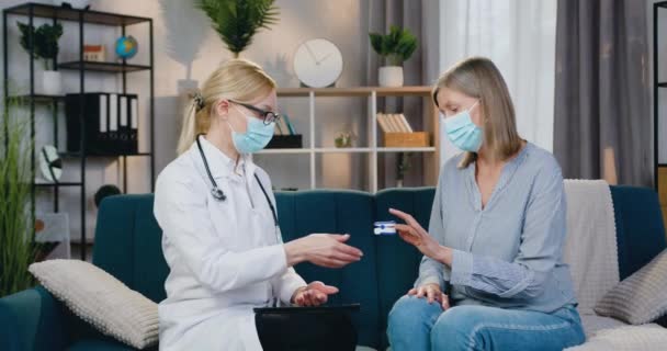 Gut aussehende blonde Ärztin in Maske misst Sauerstoffgehalt des Patienten mit modernem Messgerät bei Hausbesuchen während der Selbstisolation auf covid-19 — Stockvideo