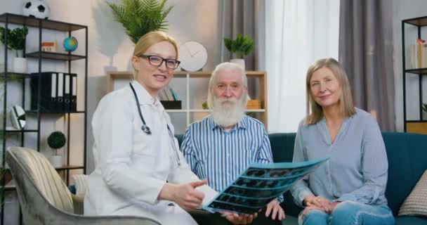 Retrato de boa aparência positiva cuidando médico qualificado feminino que segurando a varredura de raios X e olhando para a câmera com atraente casal maduro satisfeito com polegares para cima — Vídeo de Stock