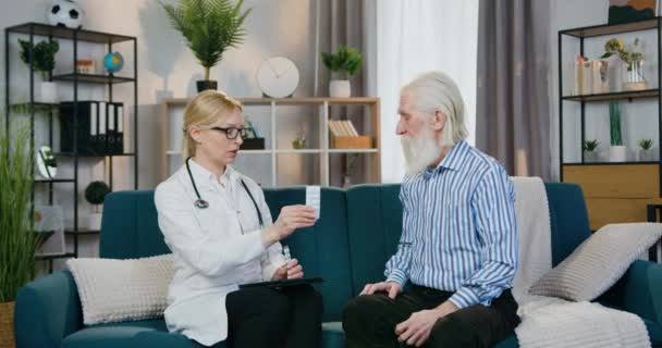 Gut aussehende, freundliche, erfahrene Ärztin gibt ihrem alten männlichen Patienten Tabletten und erzählt, wie man sie beim Hausbesuch einnimmt — Stockvideo