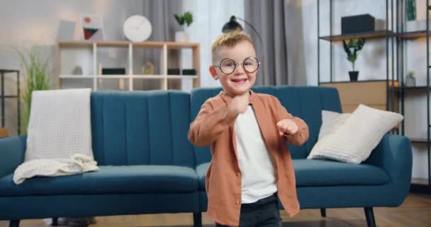 Guapo niño divertido divertido en gafas bailando en el medio de salón bellamente decodificado, vista frontal — Vídeo de stock