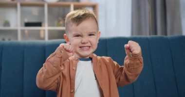 Çağdaş evdeki kanepede oturan yakışıklı, komik çocuk. Yüzünde öfkeyi resmeden ve yumruklarını kameraya dayayan çocuk.