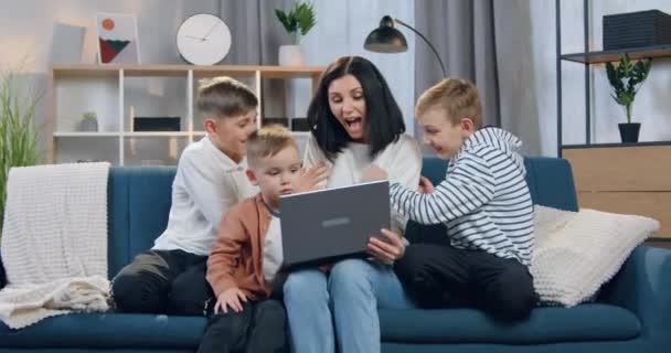 Concepto familiar donde la encantadora mujer feliz sonriente se divierte junto con sus juguetones niños de diferentes edades en casa — Vídeos de Stock