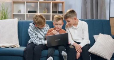Yakışıklı, neşeli iki büyük kardeş en küçük kardeşlerine laptopu evde nasıl kullanacaklarını öğretiyor.