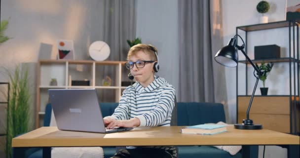 Bello eccitato ragazzo adolescente emotivo in cuffia seduto al tavolo davanti al computer e giochi, concetto di svago — Video Stock