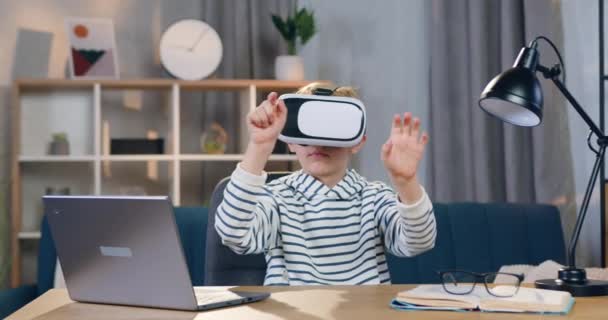 Ritratto di attraente ragazzo intelligente di 10 anni in cuffia realtà virtuale che siede sul suo posto di lavoro e lavora sullo schermo immaginario — Video Stock