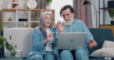 Sevimli mutlu, gülümseyen yaşlı çift video görüşmesi sırasında arkadaşlarıyla kanepede oturup el sallayarak merhaba diyor ve hava öpücüğü yolluyor.