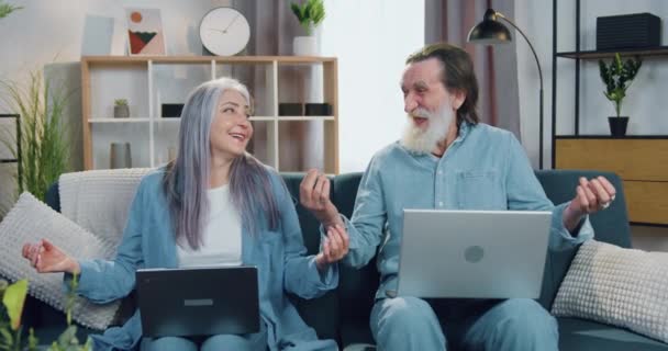 Pareja madura feliz sonriente agradable relajado en el sofá y meditando con los ojos cerrados al hacer una pausa entre la lectura de noticias en el ordenador portátil — Vídeos de Stock