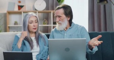 Keyfi yerindeyken mutlu olan erkek ve kadın emekliler rahat oturma odasındaki yumuşak koltukta oturup laptopta okudukları haberleri tartışıyorlar.