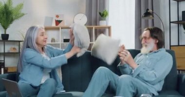 Evdeki kanepede oturup yastıklarla oynarken eğlenen ve birbirlerine sarılan mutlu ve mutlu bir çiftin portresi.