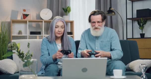 Очаровательная улыбающаяся довольная пожилая пара, наслаждающаяся победой в видеоигре и дающая друг другу пять, отмечающая совместную победу, вид спереди — стоковое видео