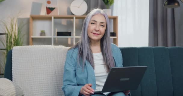 Goed uitziende glimlach zorgeloos volwassen grijs-harige vrouw zitten in de voorkant van de camera met computer en tonen duimen omhoog, close-up — Stockvideo