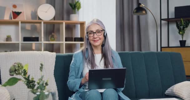 Portret van een goed uitziende vrolijke glimlachende volwassen vrouw in een headset die voor de camera zit tijdens een videoconferentie — Stockvideo