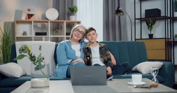 Atractiva alegre feliz amigable abuela y nieto sentado en el sofá en casa y mirando a la cámara con sinceras sonrisas, vista frontal — Vídeos de Stock