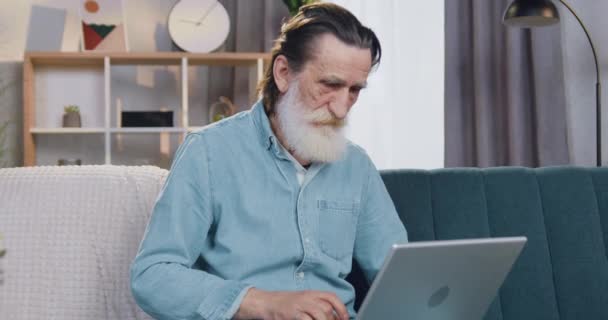 Attraktiv på gott humör säker typ senior skäggig man som arbetar på laptop hemma och tittar på kamera med tummen upp, framifrån — Stockvideo