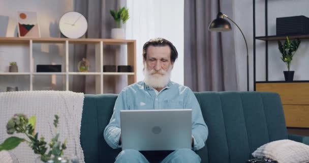 Snygg säker trött seniorskäggig man sitter framför datorn och mediterar med slutna ögon för att njuta av harmoni i kroppen och tystnad runt — Stockvideo