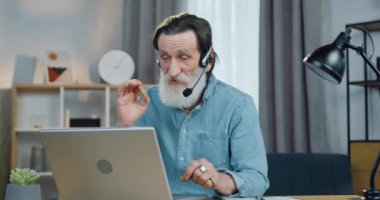 Kendinden emin, sakallı, kulaklık takmış yaşlı, çekici bir öğretmen. Evde yaşayan dinleyicilerle veya öğrencilerle online dersler veriyor. Uzak eğitim kavramı.