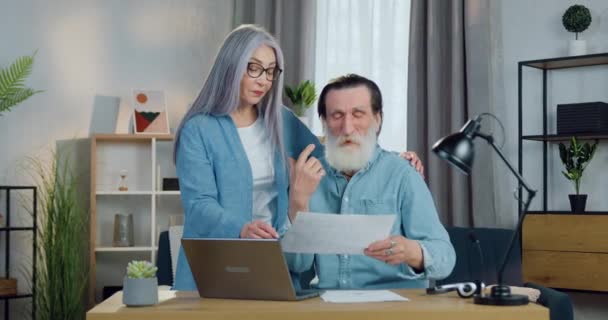 Attractive positive happy male and female pensioners talking at the table in cozy room and discussing report about family costs — Stock Video