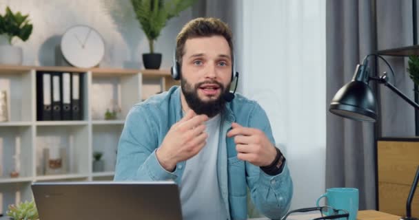 Likable fiducioso successo 30-aged blogger maschile con barba elegante in cuffia registrazione stile di vita vblog per i suoi seguaci seduti di fronte alla fotocamera a casa — Video Stock