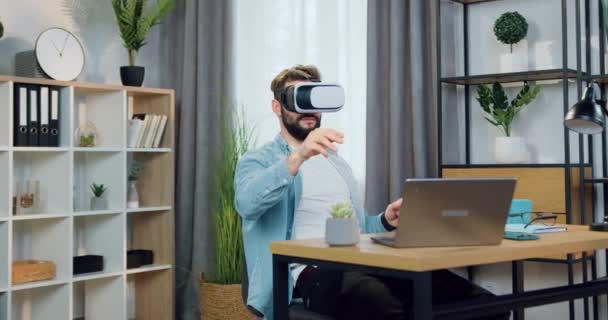 Attraktive zuversichtlich in guter Laune bärtigen Kerl in Augmented-Reality-Brille arbeiten auf imaginären Bildschirm in schön dekorierten Home Office — Stockvideo