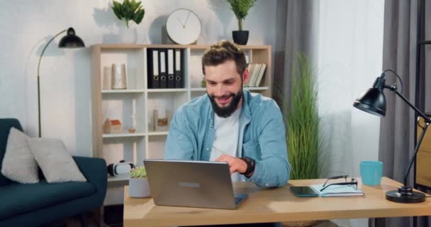 Dobře vypadající spokojený zkušený vousatý chlap sedí v uvolněné póze v křesle s rukama za hlavou po úspěšné práci na počítači doma — Stock video