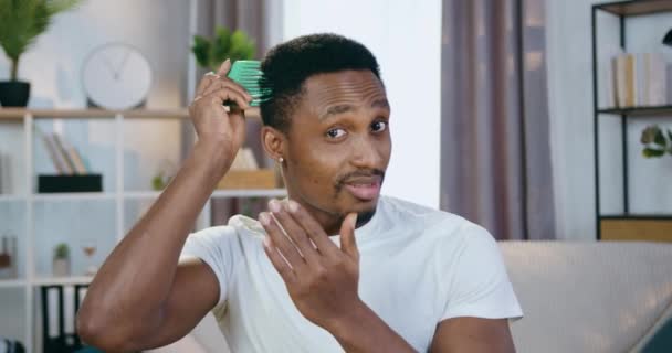 Portrait of good-looking smiling confident young african american which combing his hair with special comb and looking into camera with satisfied face expression — Stock Video