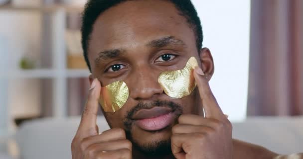 Можливо, в гарному настрої сучасний молодий чорношкірий чоловік позує в камеру з золотими колагеновими окулярами, концепція догляду за обличчям — стокове відео