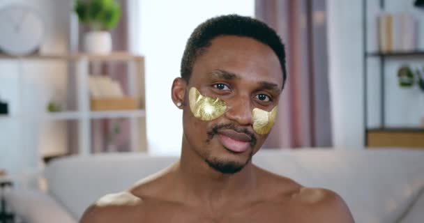 Handsome smiling modern young half-naked african american looking at camera with collagen refreshing patches under eyes,face care concept — Stock Video