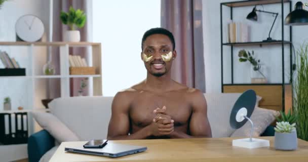 Kosmetische Gesichtsbehandlung Konzept, bei dem gut aussehende lächelnde junge schwarzhäutige nackte Kerl posiert in die Kamera mit goldenen erfrischenden Augenklappen — Stockvideo