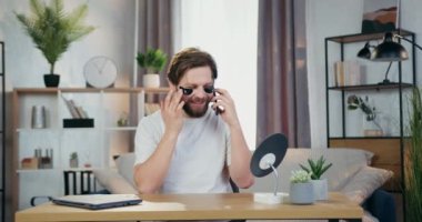 Yakışıklı, 30 'lu yaşlarda sakallı, kolajen tazeleyici bantları olan, gözlerinin altında küçük bir aynanın önünde oturan ve cep telefonuyla konuşan biri.