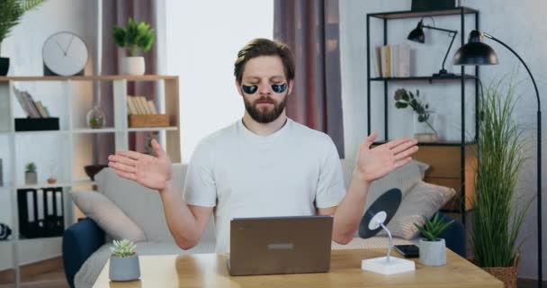 Attractive caring young relaxed bearder with anti-aging black eye-patches sitting with mudra hands at his workplace and meditating with closed eyes — Stock Video